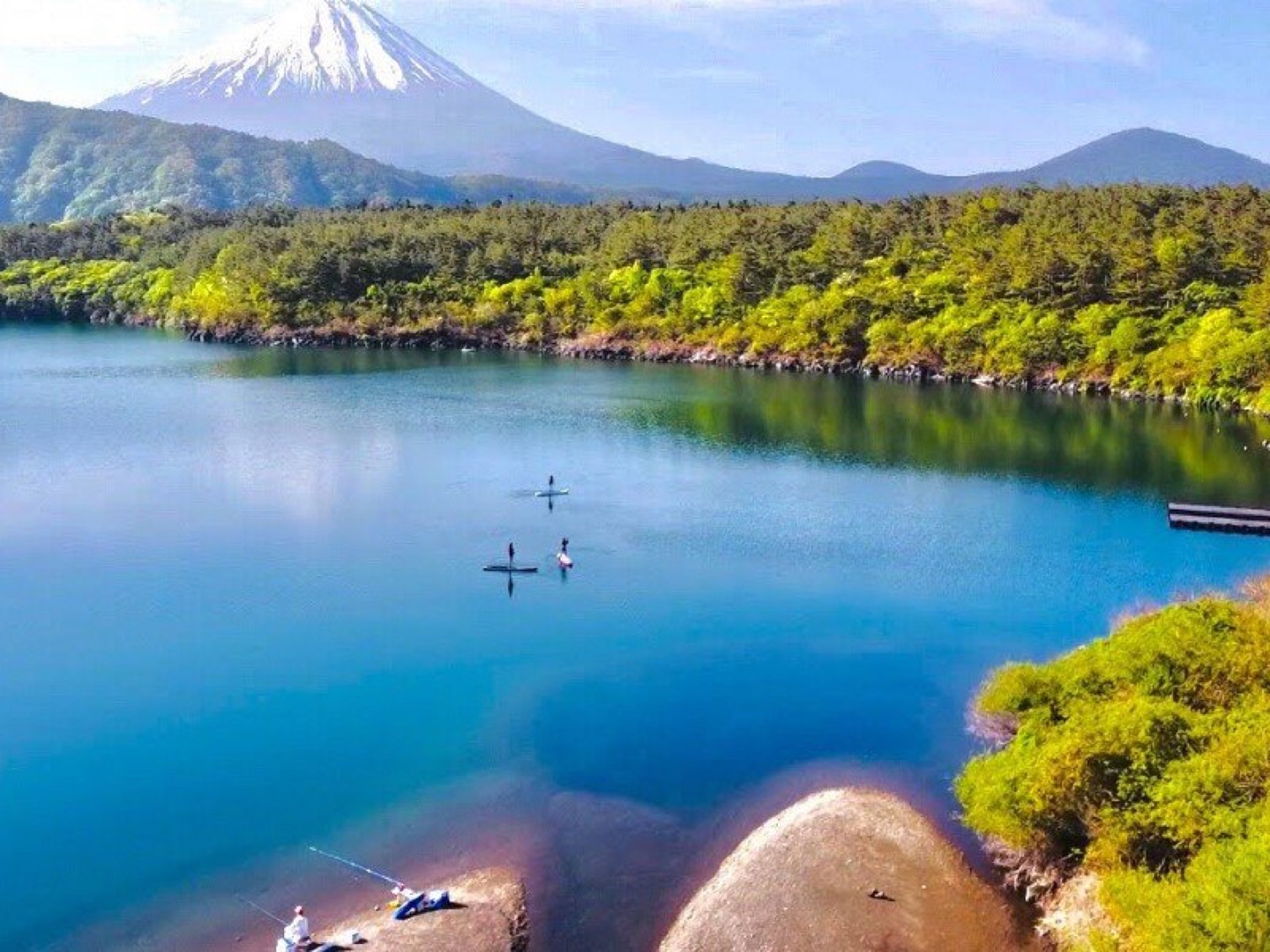 富士山を背に、青く澄んだ西湖の上でSUPのボードに立つ人たち